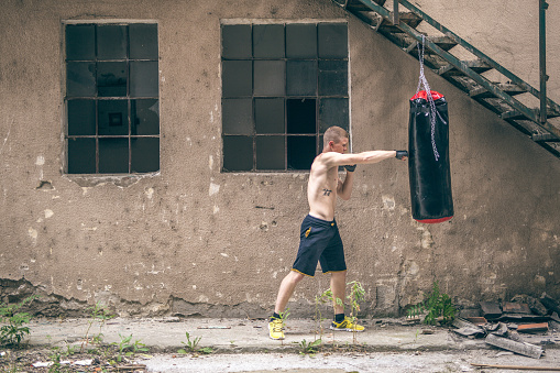 years old male training outdoors. He is kicking and punching boxing bag